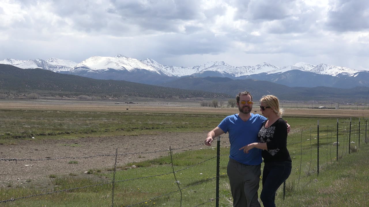 Couple standing by a wire fence with snowy mountains behind them.