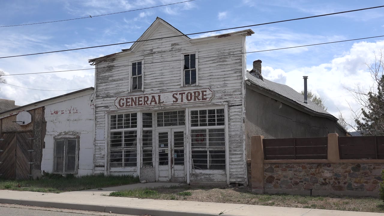 Weathered white general store facade beside a brick fence.