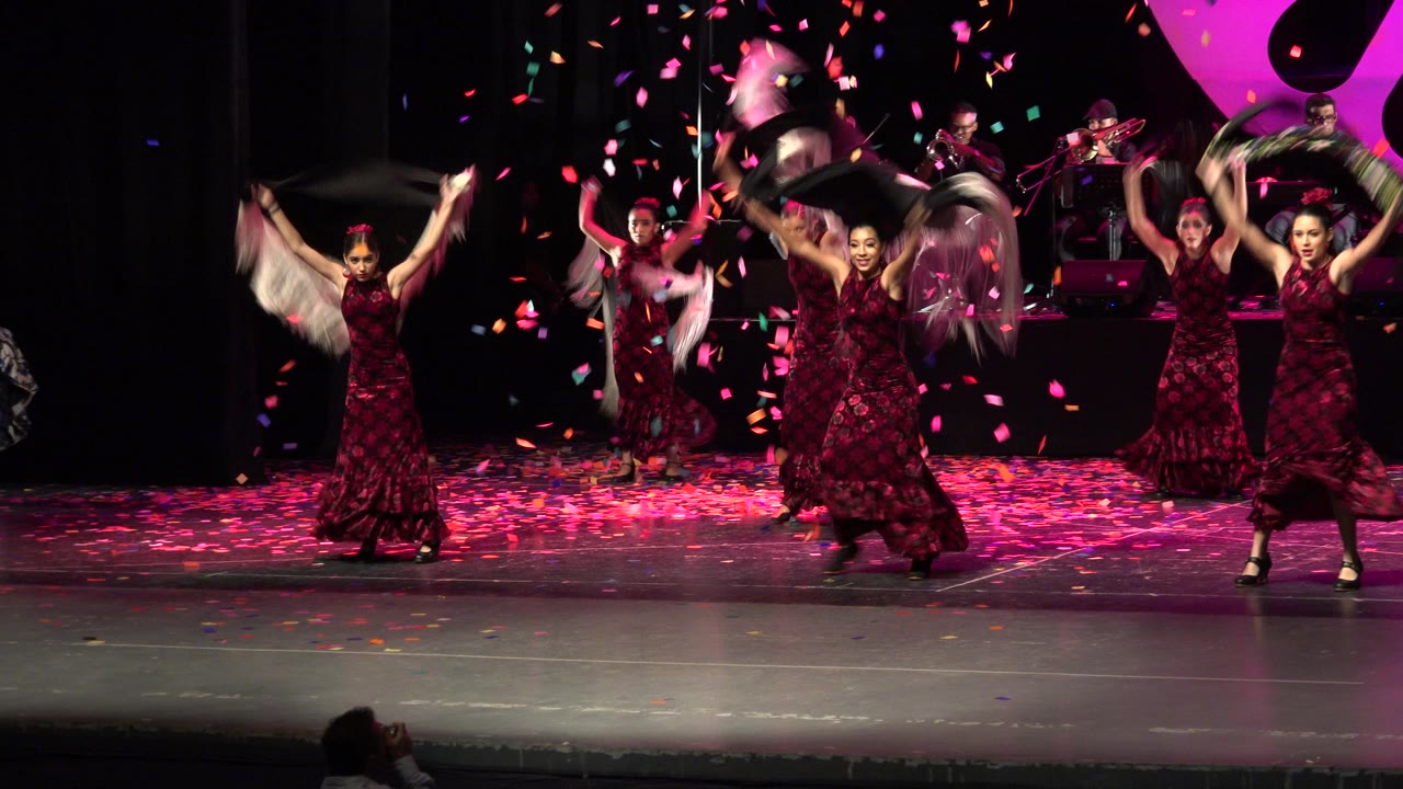 Dancers in red dresses perform on a stage with confetti falling.