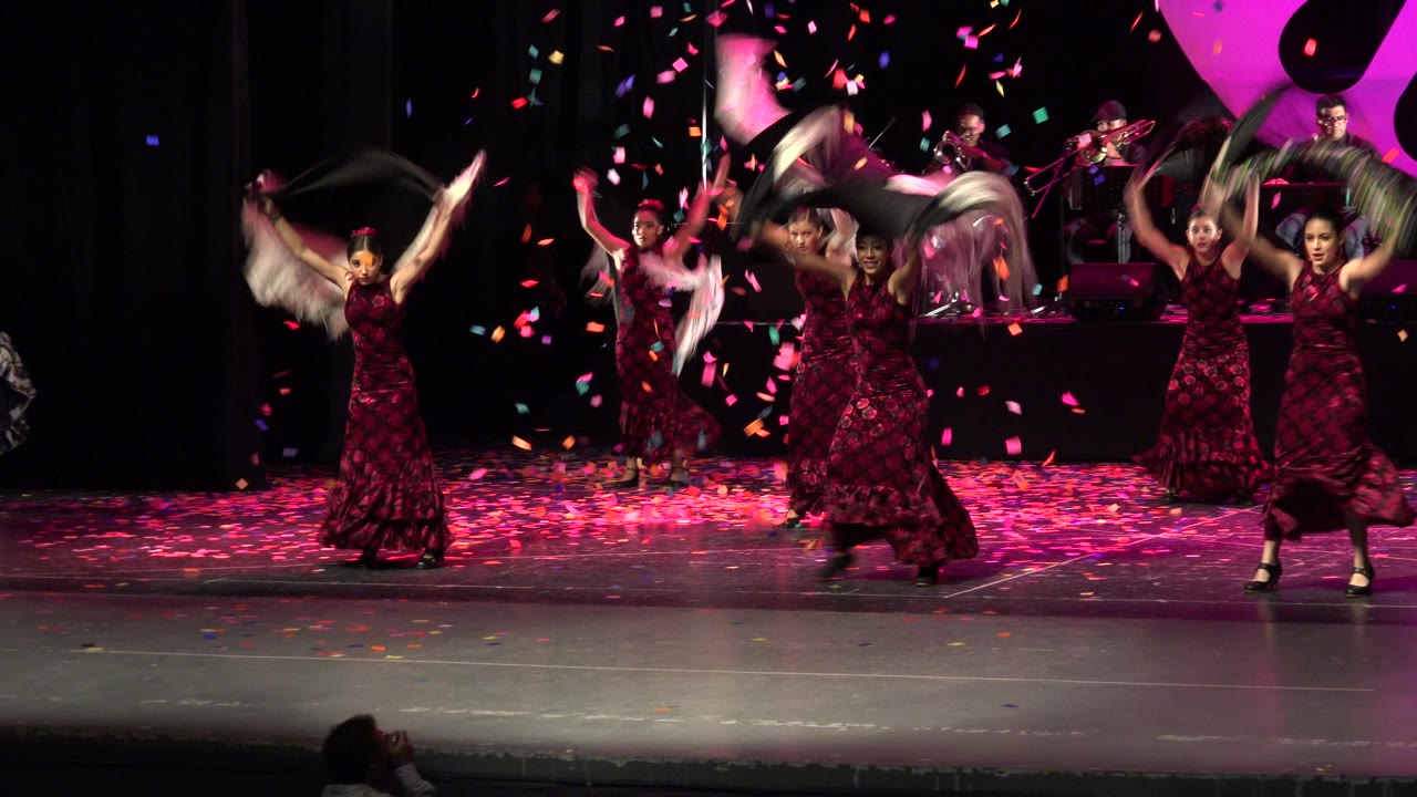 In Cabo San Lucas, Mexico, the dancers lift shawls and fringe scarves during the stage routine, with bright confetti scattered across the air and floor.