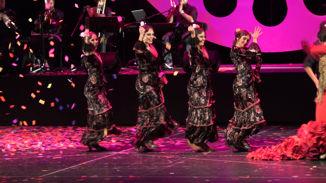 Dancers move in a line across a confetti-covered stage.