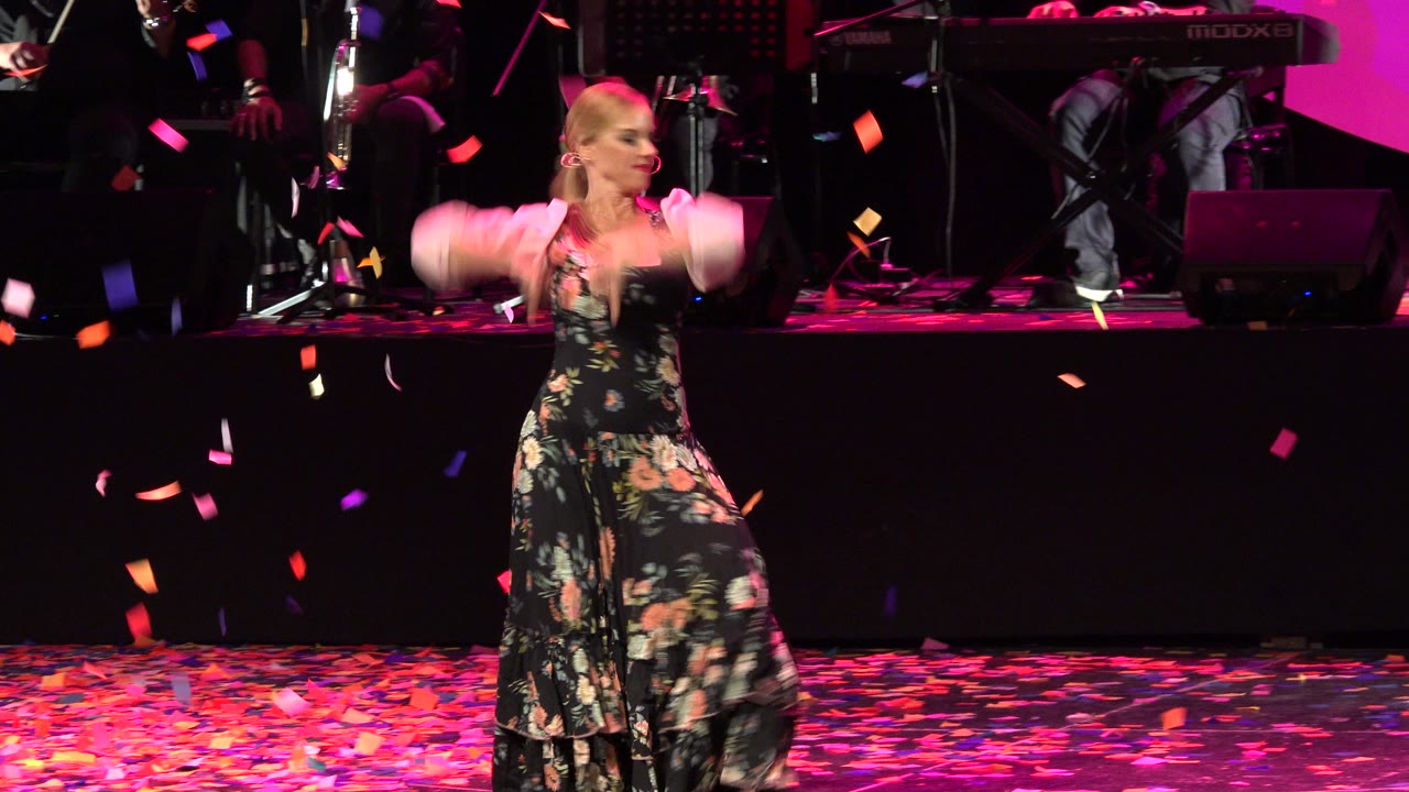 Woman in floral dress dancing on a petal-covered stage.