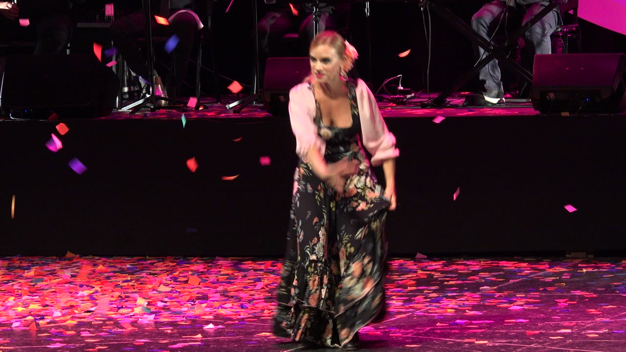 Woman dancing on a dark stage as confetti falls.