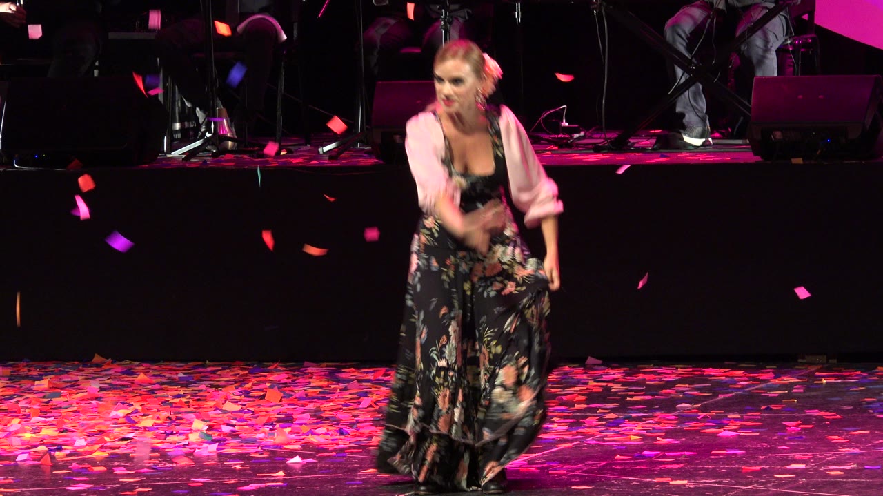 The performer faces forward in Cabo San Lucas, Mexico, with colorful confetti suspended in the air and a dark band riser behind her.