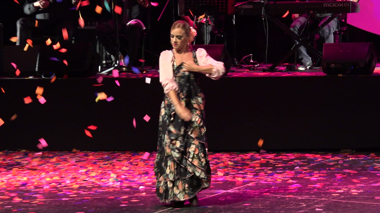 Woman dancing on a confetti-covered stage with musicians behind her.