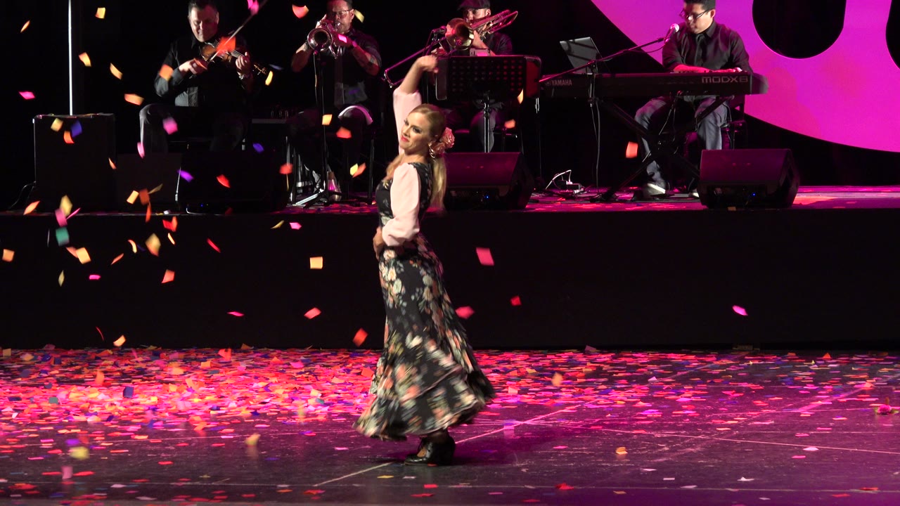 Woman dancing on a confetti-covered stage with musicians behind her.