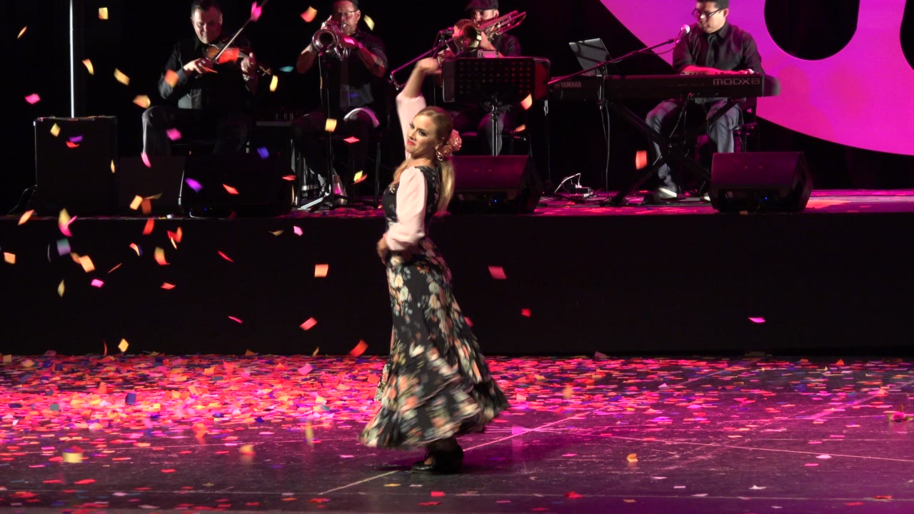 The dancer turns across the dark stage in Cabo San Lucas, Mexico, as colored confetti falls in front of seated musicians.