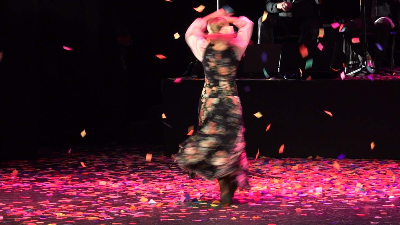 Woman in floral dress spinning on a confetti-covered stage.