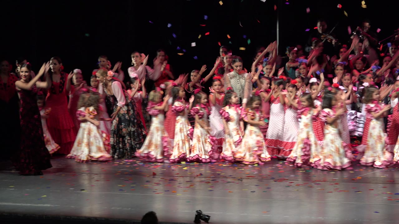 A second wide stage moment in Cabo San Lucas, Mexico, shows girls in red, pink, and floral dresses clapping while the group shifts slightly under stage lights.