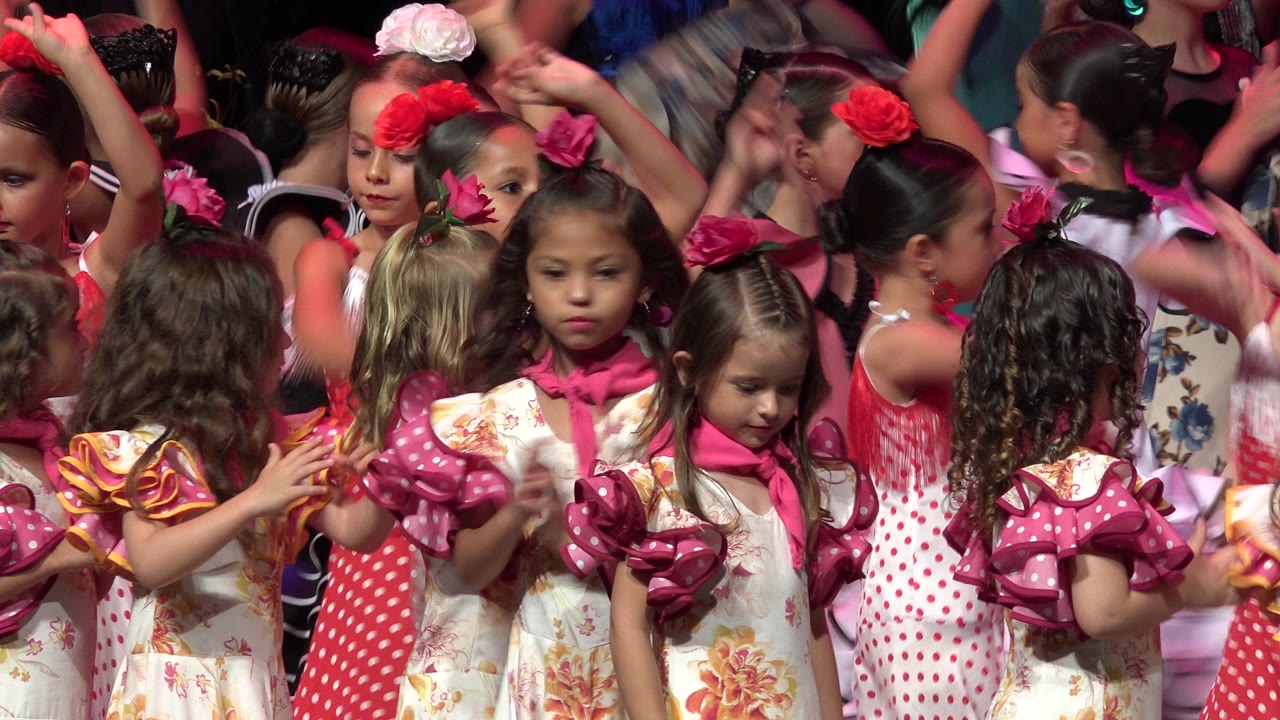 Young girls in pink and floral dance costumes crowd a stage.