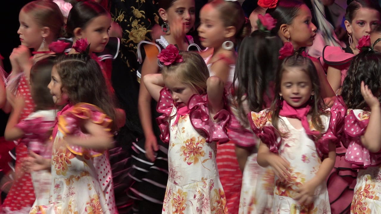 Young girls in pink and floral costumes gathered on a stage.