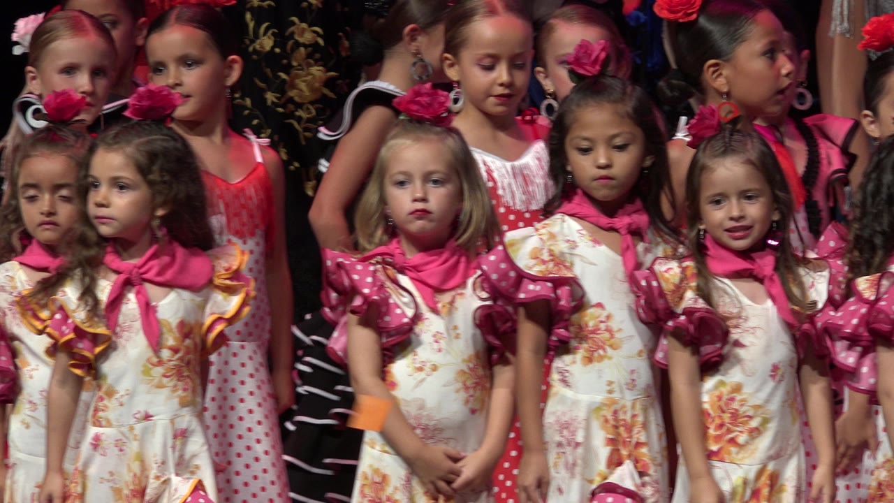 Several young girls face forward in matching floral costumes while other children in red and black outfits stand behind them in Cabo San Lucas, Mexico.