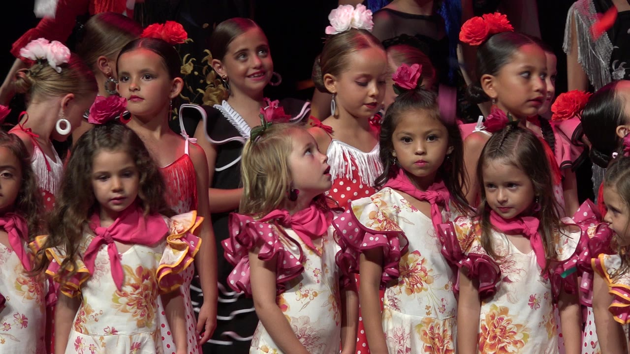 Several young girls in pink, red, and floral dresses look around while standing together in Cabo San Lucas, Mexico, with faces clearly visible.
