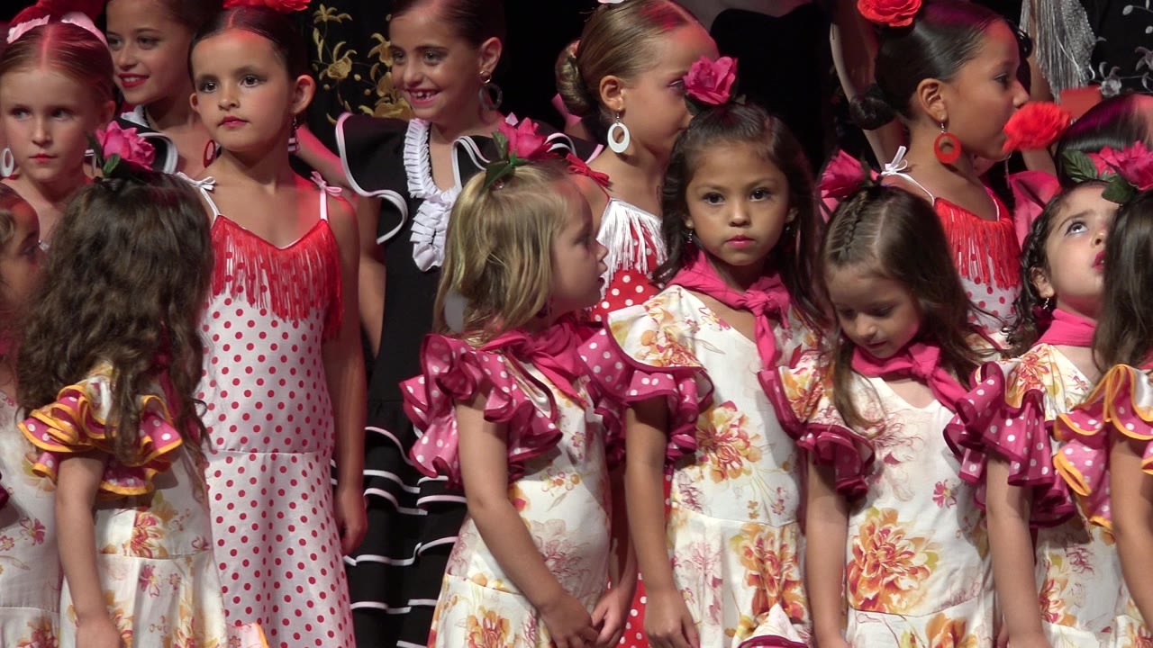 Young girls in colorful performance dresses stand closely together.