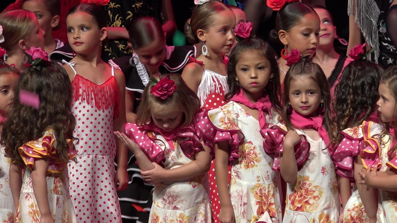 A young girl in a floral dress looks toward the camera among other girls.