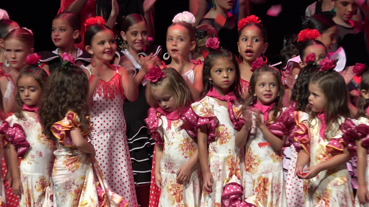 A tight stage view shows girls in red polka-dot and floral costumes clapping while facing the audience in Cabo San Lucas, Mexico.