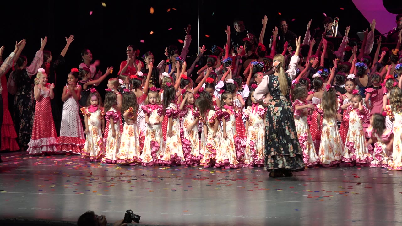 Wide performance frame in Cabo San Lucas, Mexico, with a dense row of girls in floral dresses and pink accessories facing the audience under stage lighting.