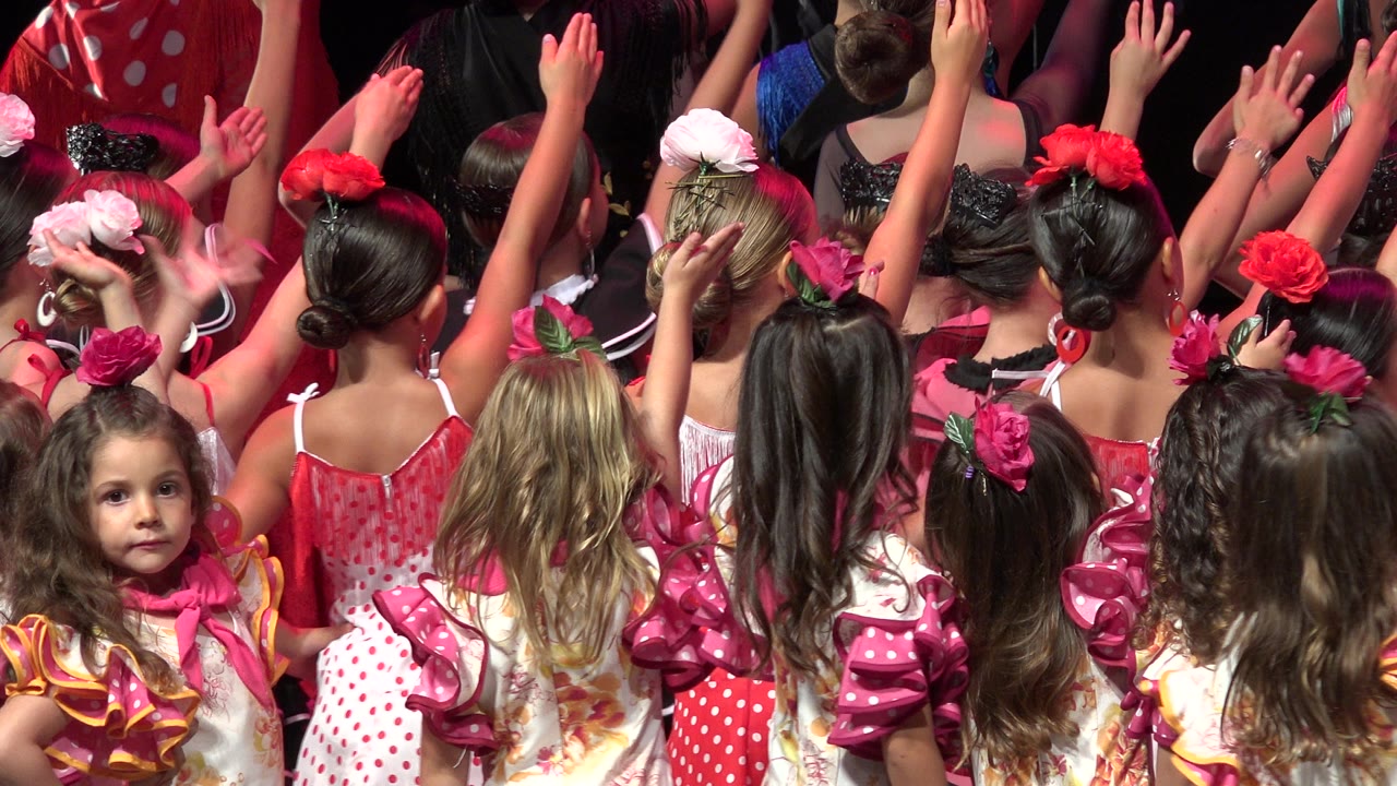 Children in bright costumes raise their arms on a stage.
