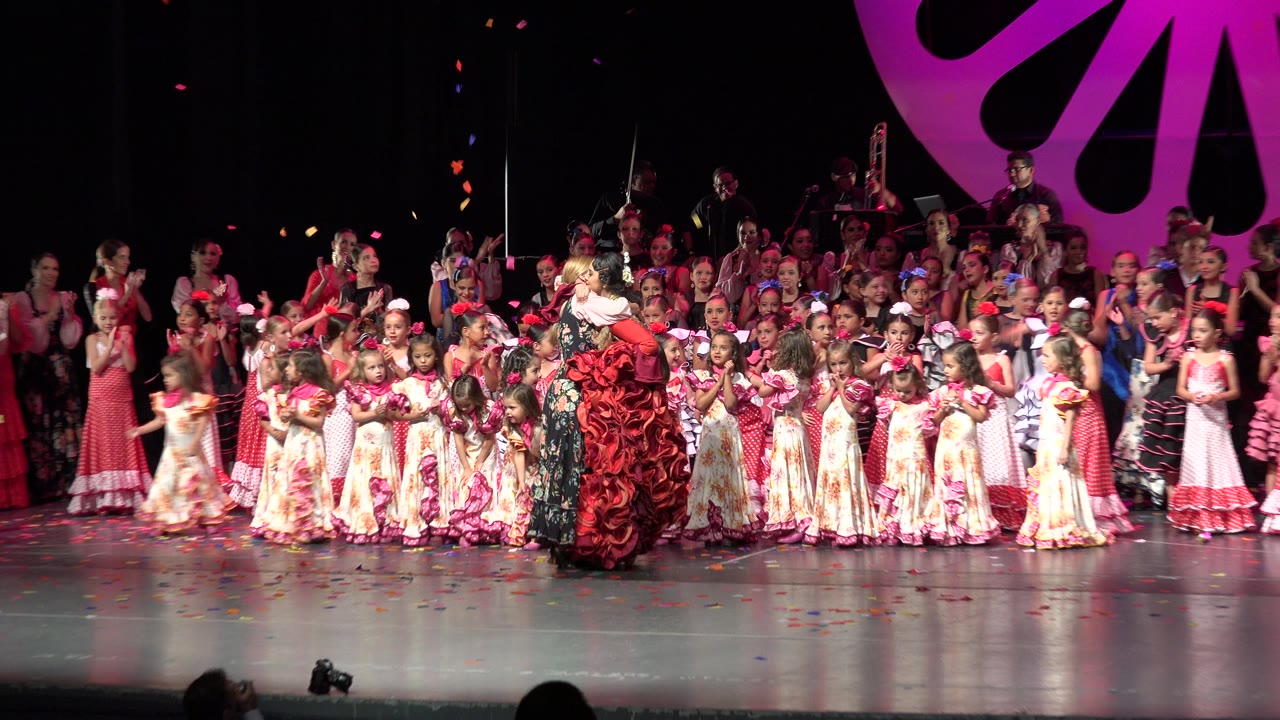 Wide stage view of two women hugging amid a large crowd of children and adults.