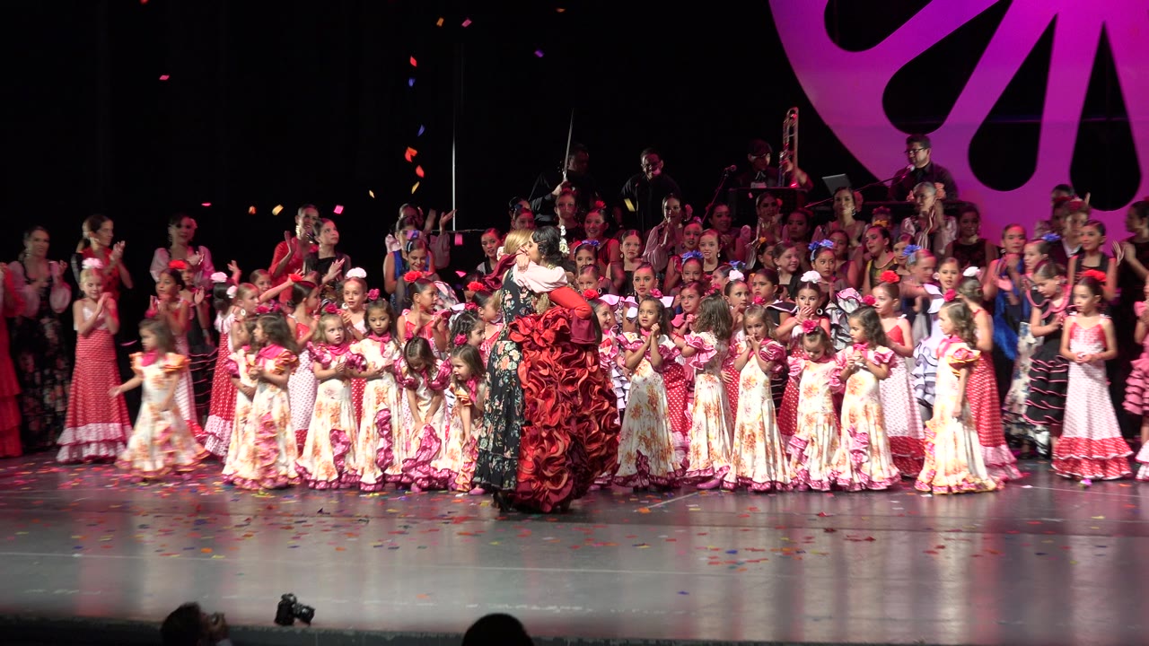 A second wide moment in Cabo San Lucas, Mexico, keeps the women hugging at center while the surrounding children face different directions under stage light.