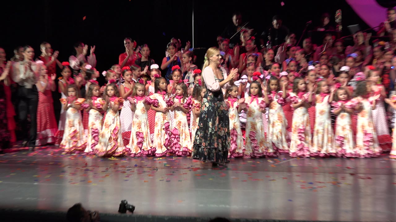 Wide stage crowd with blurred adult movement near children in dresses.
