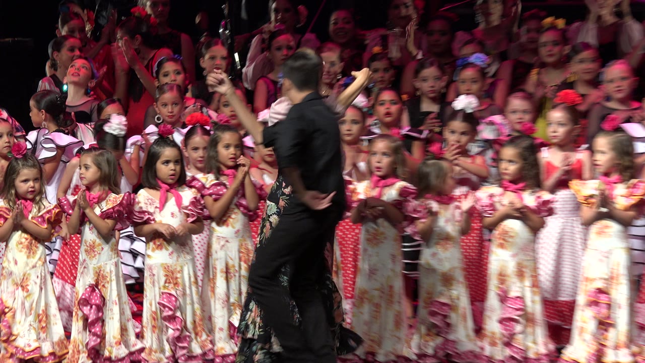In Cabo San Lucas, Mexico, the man crosses the foreground in motion blur while rows of costumed children clap and watch from the stage background.