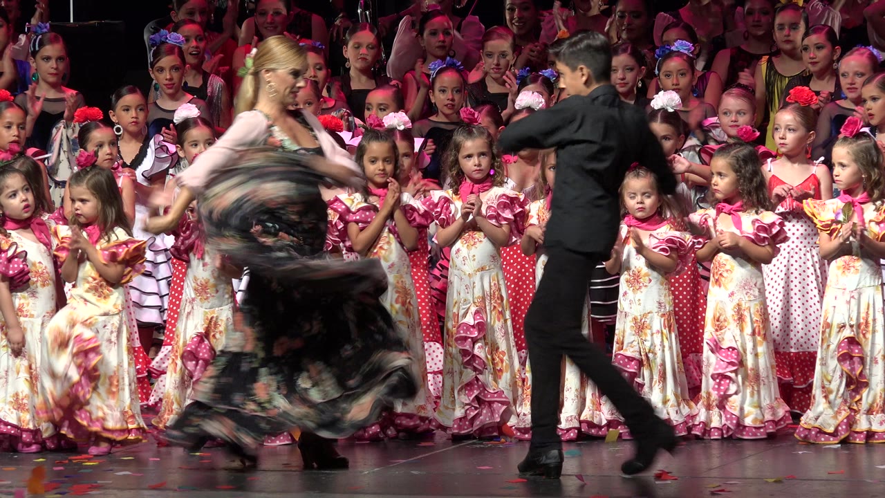 Adult dance couple onstage in front of children in pink costumes.