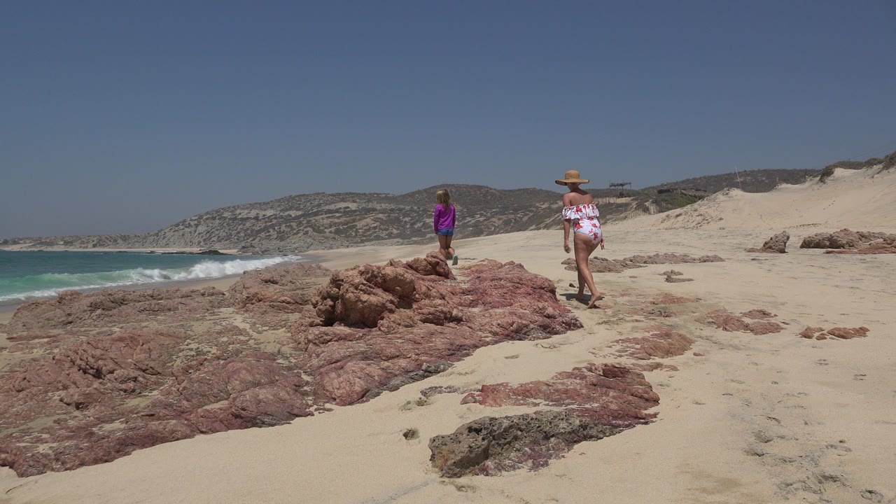 Woman and child on sandy beach rocks beside ocean surf.