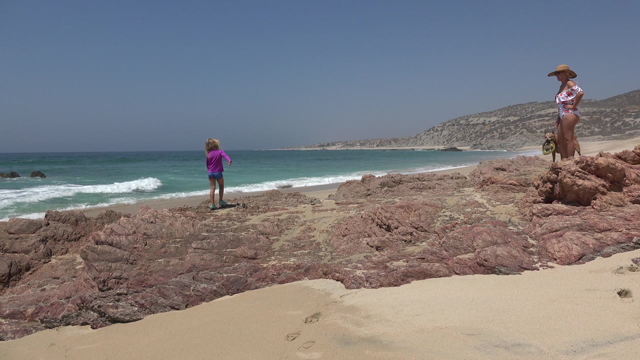Child and adult on rocky beach above surf.