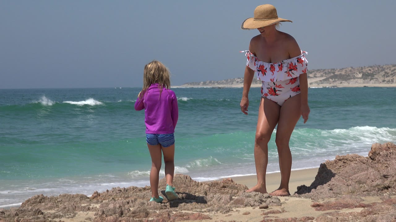 Woman and child standing on rocky beach near surf