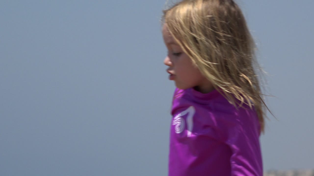 Young girl in a purple swim shirt in profile against blue sky.
