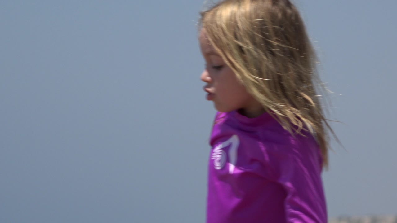 A similar close side angle keeps the young girl in purple near the center of the frame, with windblown hair and an uncluttered sky behind her in Cabo San Lucas.
