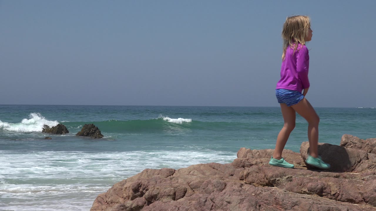 Child walking on rocks above the surf.