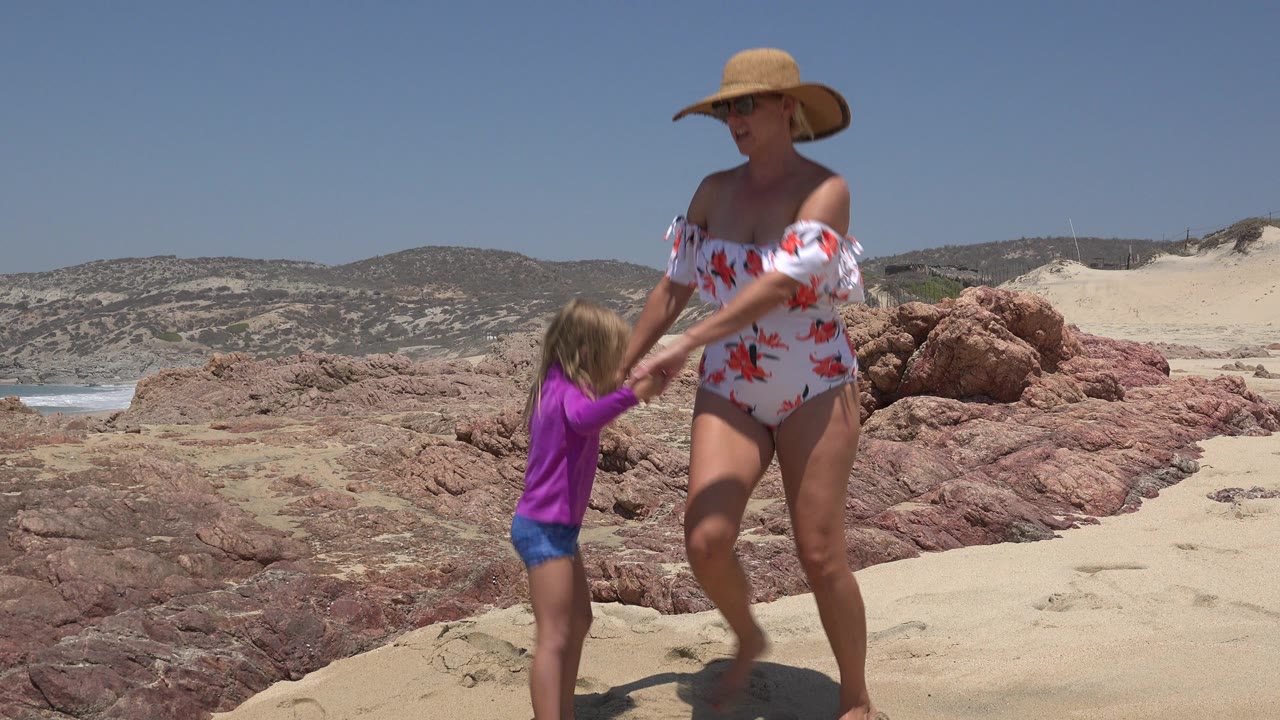 Woman and young girl holding hands on a sandy beach.