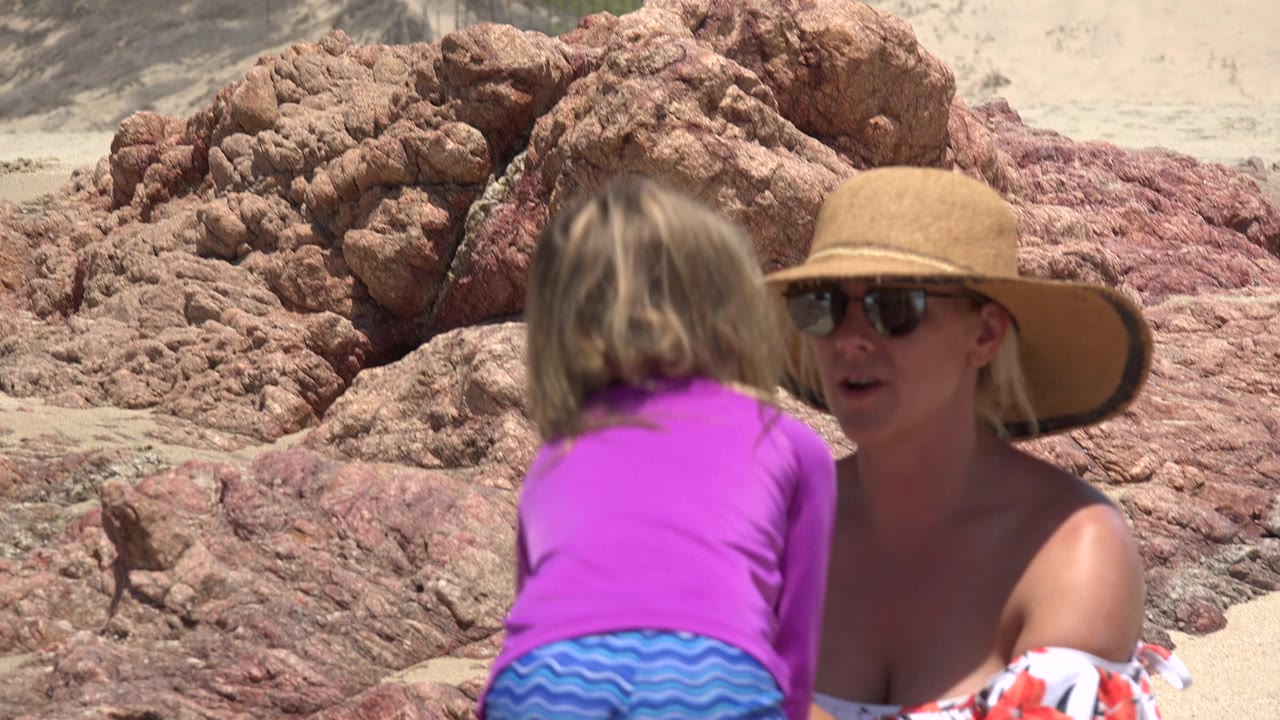 Woman in sun hat faces a child in purple near red rocks.