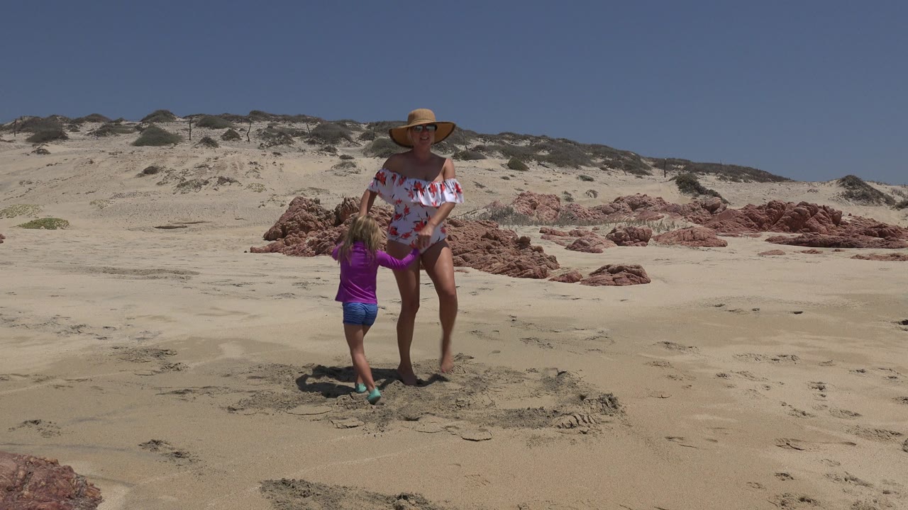 Woman and young child standing on sandy beach near red rocks