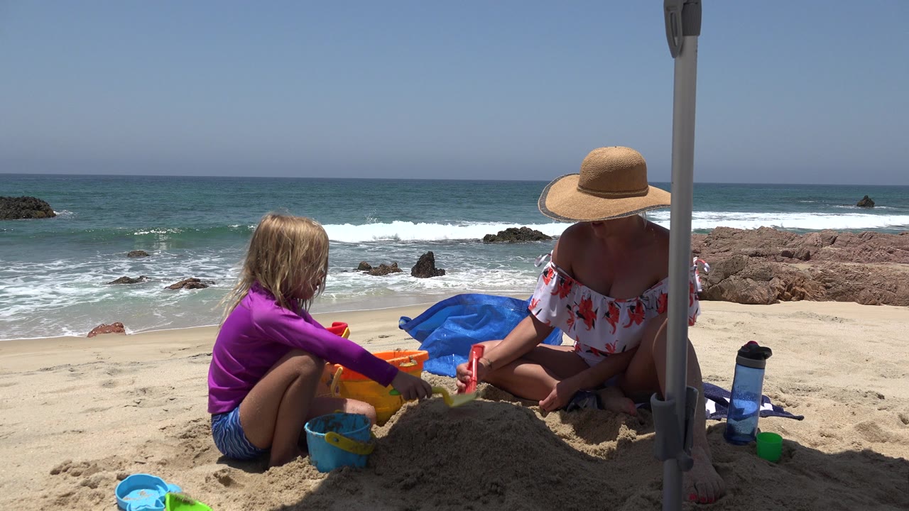 Woman and child building sandcastles on a beach beside ocean waves.