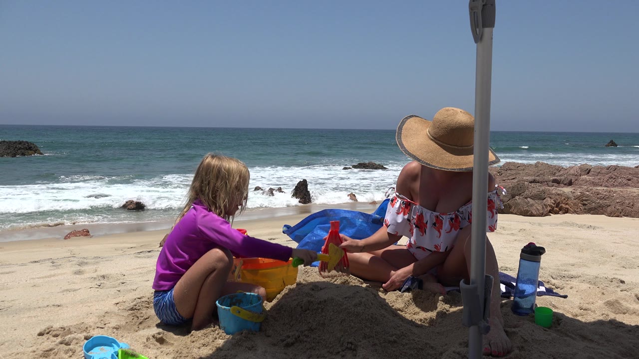 Child and adult handle bright sand toys on a sunny beach.