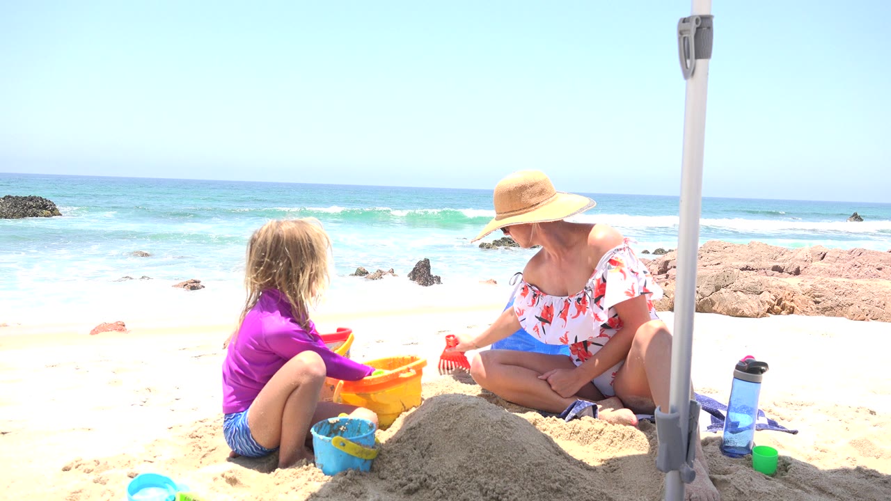 Woman and child playing with sand toys on a bright beach.