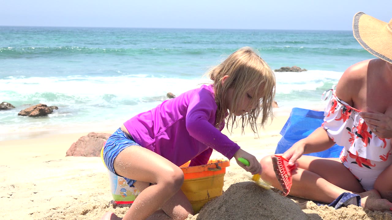 Child and woman building a sandcastle beside the ocean