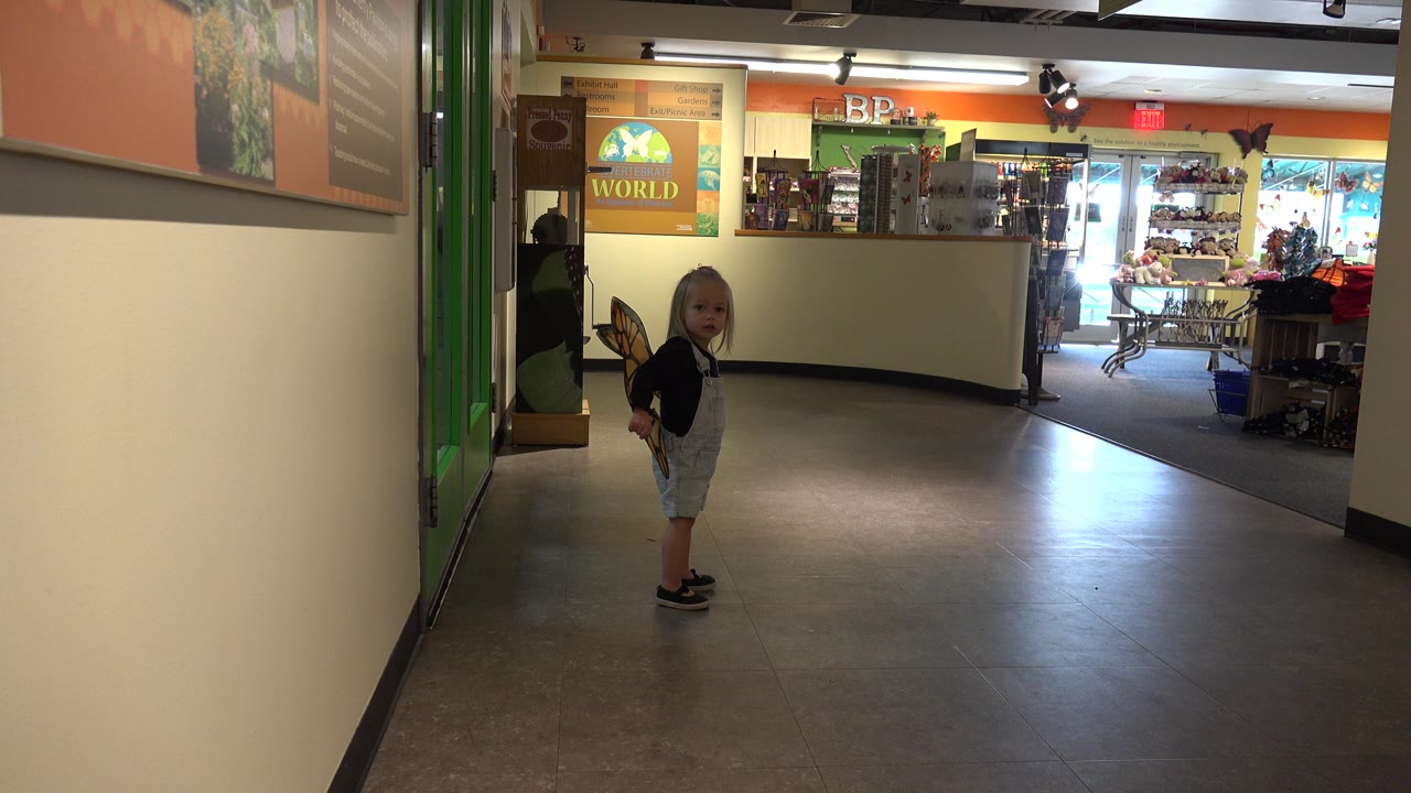 Young child wearing butterfly wings in an indoor hallway.