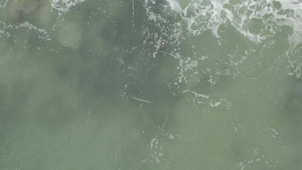 Overhead view of green ocean water in Baja California Sur, Mexico, with broken white froth near the top edge and no visible people.
