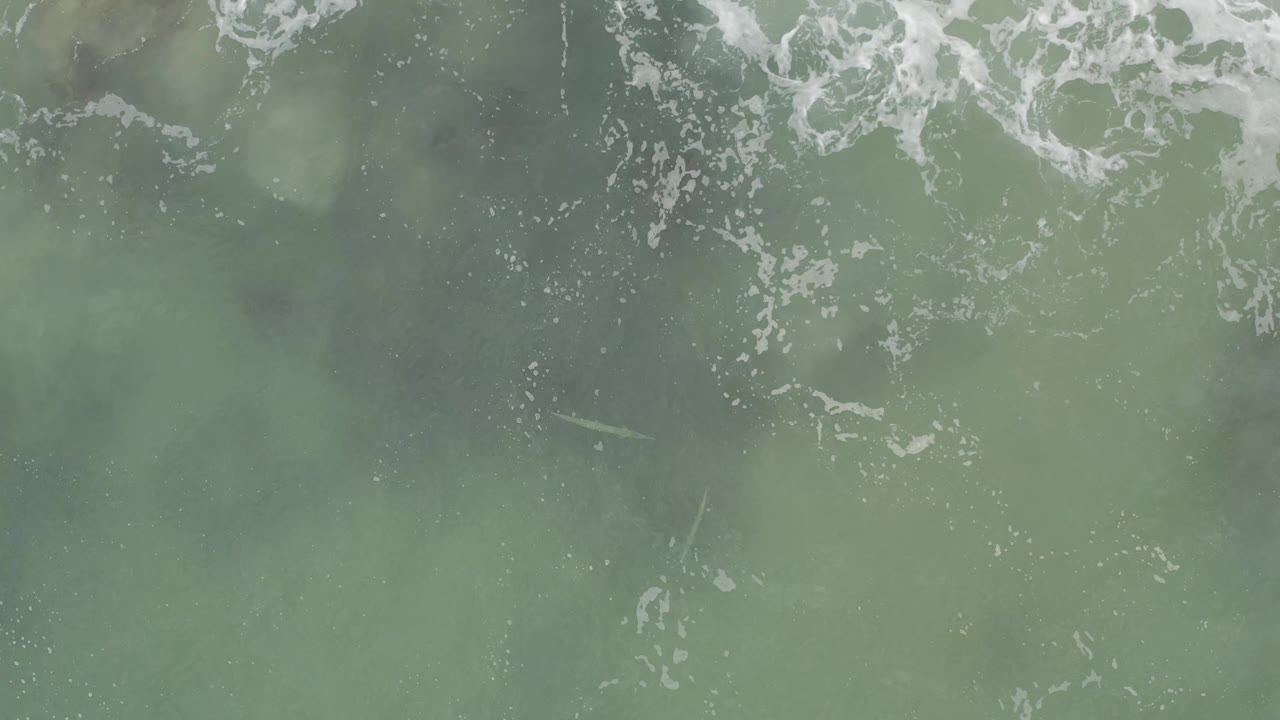 Green surf seen from above with pale foam streaks near the upper left.