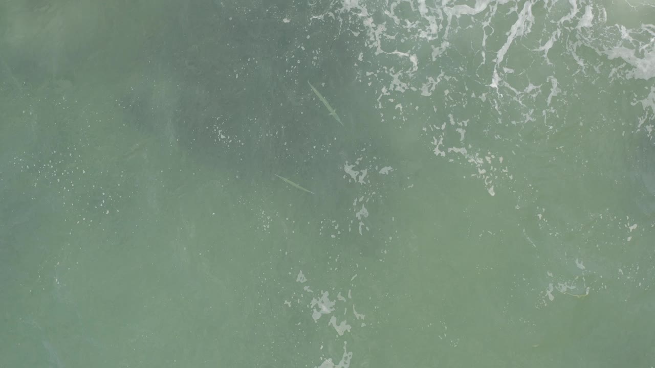 Top-down view of green sea water in Baja California Sur with white foam lines near the upper edge and no visible people.