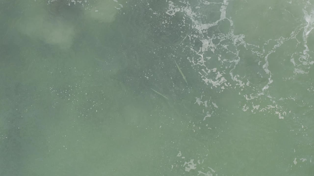 Aerial view of Baja California Sur ocean water with white foam clusters crossing the upper part of the frame and no visible people.