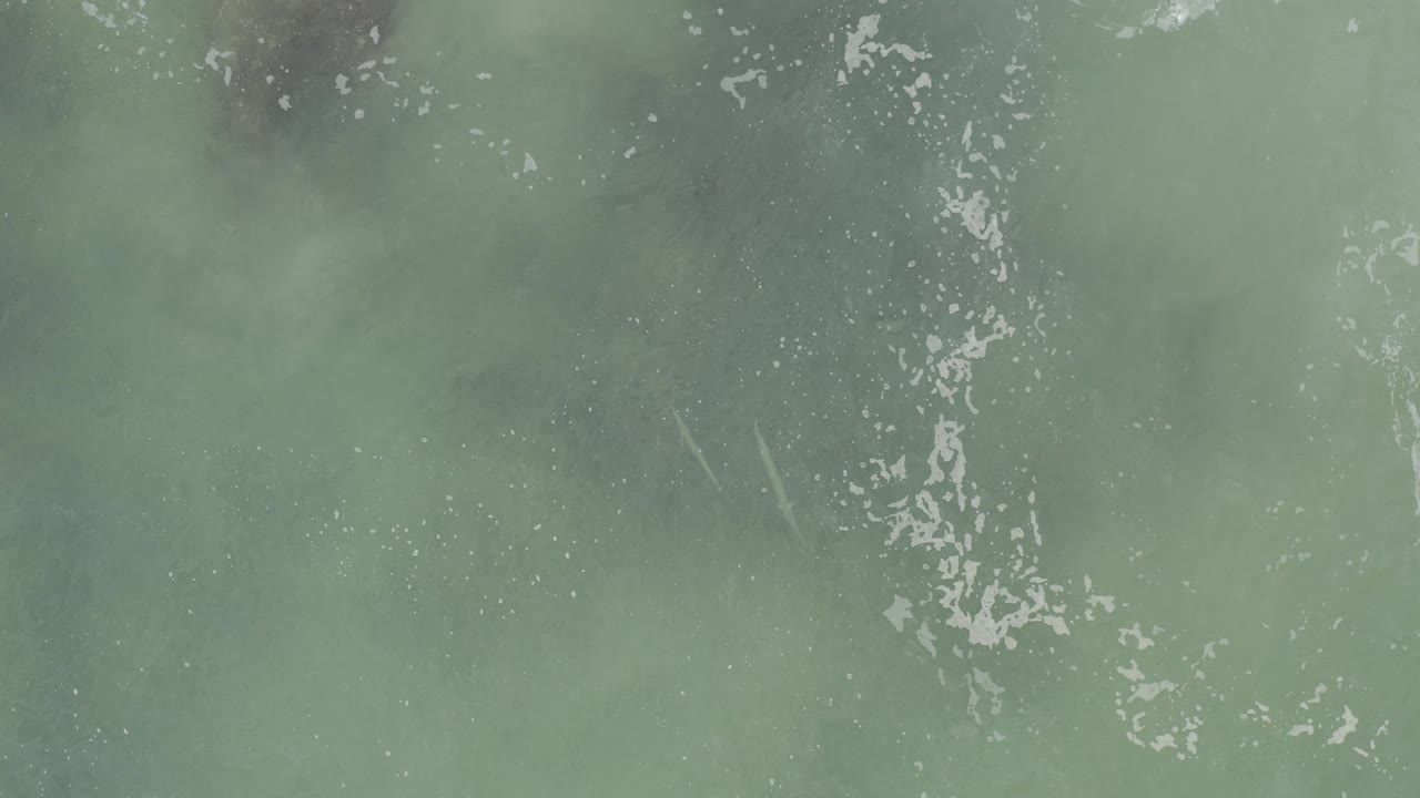 Blue-green ocean water in Baja California Sur, Mexico, seen from above with a narrow vertical trace of white foam and no visible people.