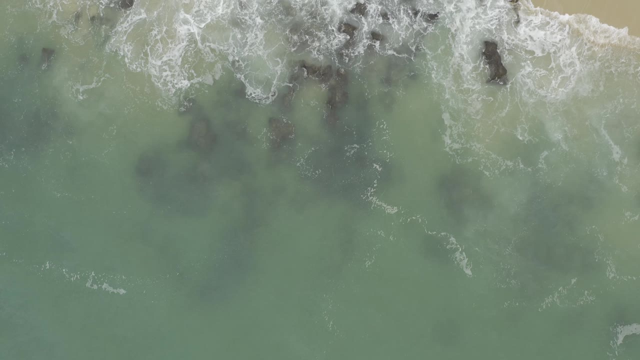 Waves wash over rocky outcrops beside a small strip of sand.