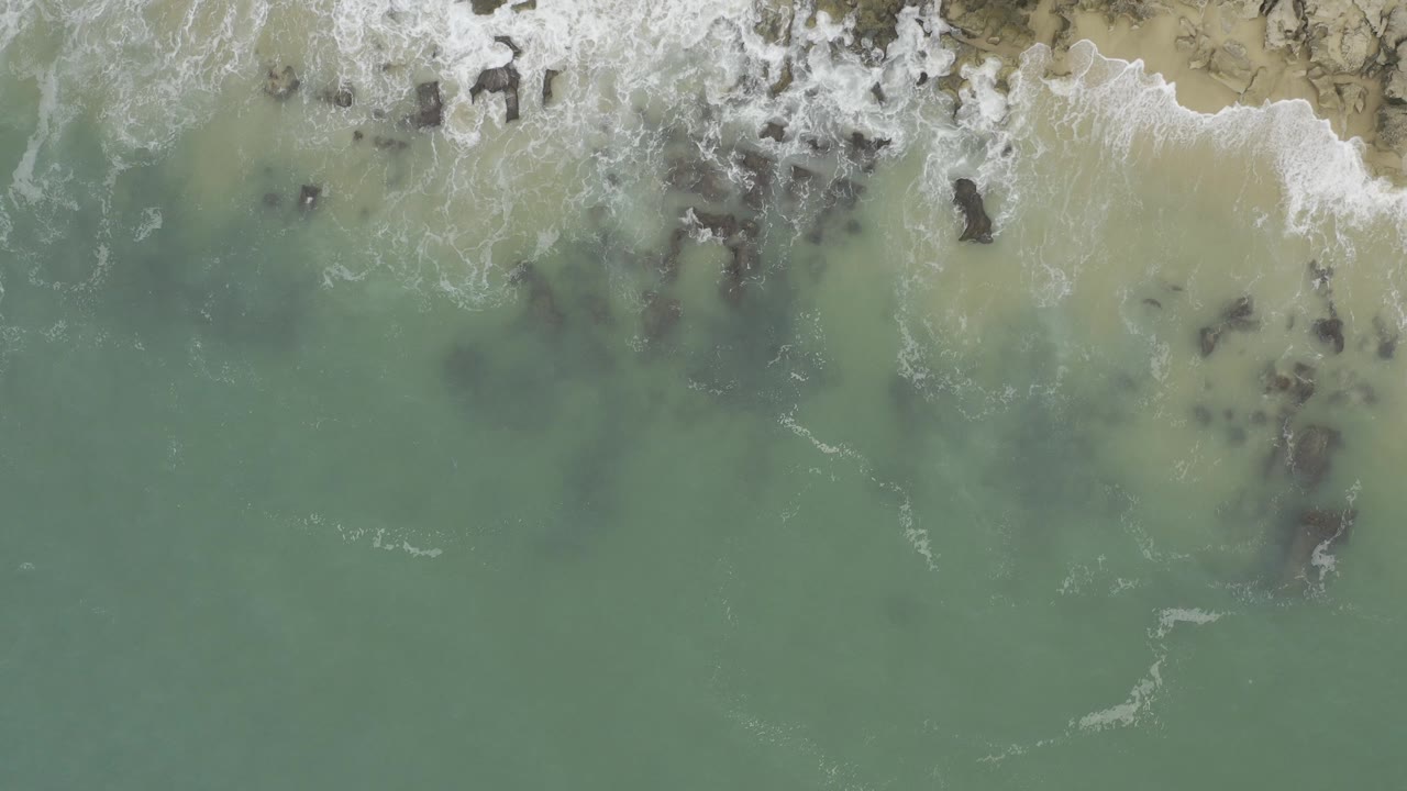 Overhead surf washing across rocks and sand