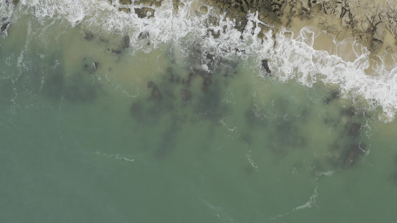 Overhead view of green ocean water and surf over a rocky shore
