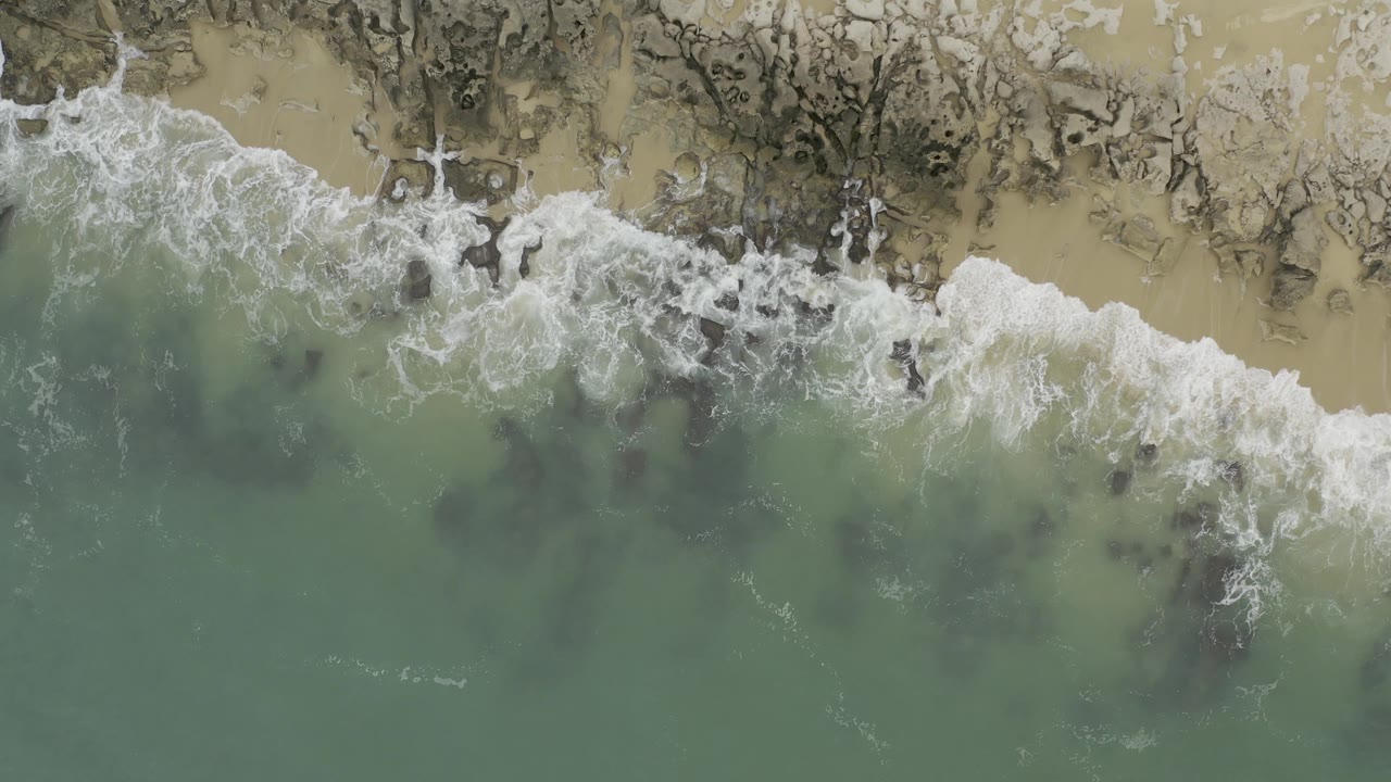 White wave foam spreads over shallow rocks beside green water.